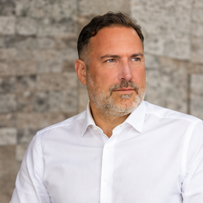 Carsten Meyer im weißen Hemd vor einer hellen Steinwand, mit Blick zur Seite.